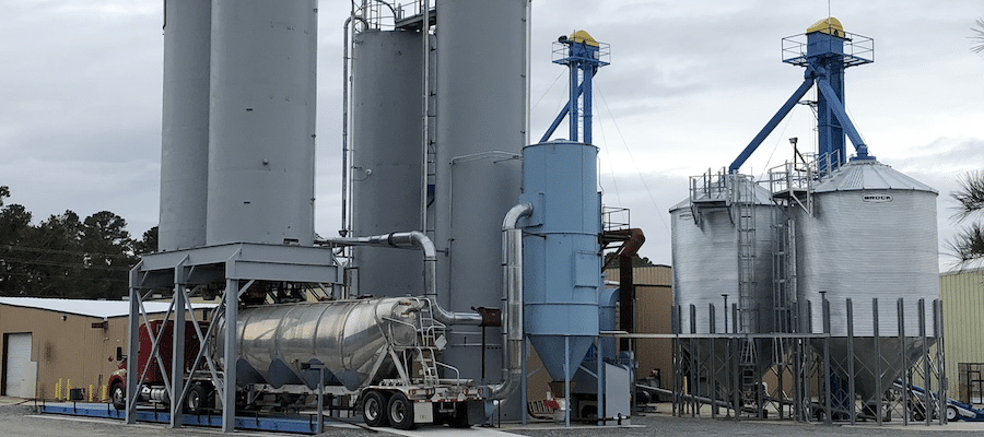 Outdoor industrial facility with storage silos, dust collection equipment, and a pneumatic tanker truck utilizing material characterization techniques for bulk powder handling.
